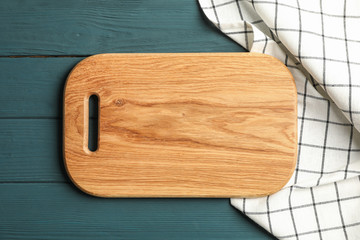 Kitchen towel with cutting board on wooden background, top view