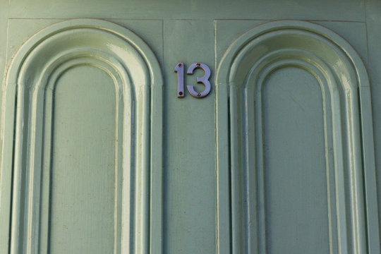 Lucky Or Unlucky House Number 13 With The Thirteen In The Middle Between Two Carved Arches Of Wood On A Light Green House Door