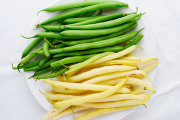 Yellow and green raw fresh beans in a white plate top view space for text vegan food