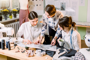 Obraz na płótnie Canvas Three attractive young fashion designers carefully creating new fashionable styles of pants. Dressmakers making clothes. Fashion, dressmaker, sewing concept