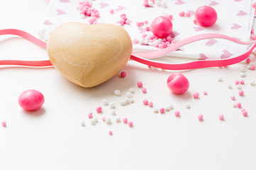 close up wooden heart with pink white aniseed, Dutch Muisjes, on white table