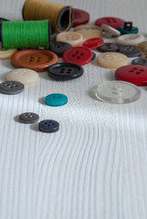 Top view of colored buttons and spools of thread on white wooden background with copy space