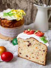 Easter cake kulich. Traditional sweet bread decorated meringue, yellow daffodils on gray background with lace fabric and colored eggs. Copy space, selective focus.Slice of cake.season's greetings card