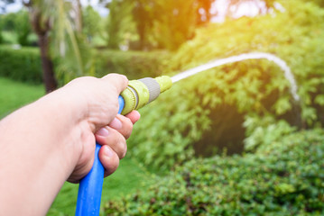 Gardener watering form blue water hose in garden