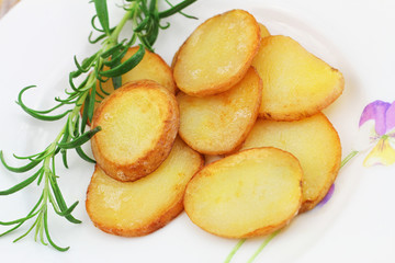 Crunchy fried potato slices with peel with fresh rosemary on white plate