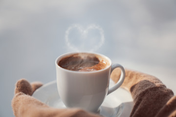 Female hands in mittens holding cup with hot  coffee