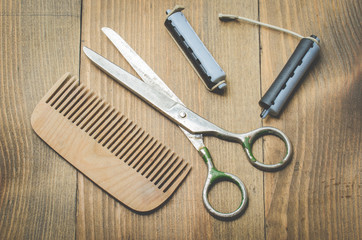 hairbrushes, curlers and a scissors on a wooden board, top view