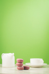 sweet macaroons or macaron and coffee cup and white creamer on a green background with copy space.  French dessert