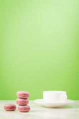 sweet macaroons or macaron and coffee white cup on a green background with copy space, selective focus French dessert