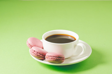 sweet macaroons or macaron and coffee white cup on a green background, close up. French dessert