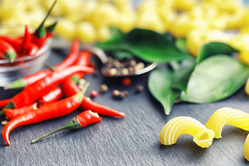 Uncooked pasta on a stone background. With seasonings and spices, spicy chili peppers.