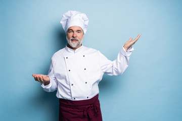 Portrait of a happy chef cook showing copyspace on the palms isolated on light blue background.