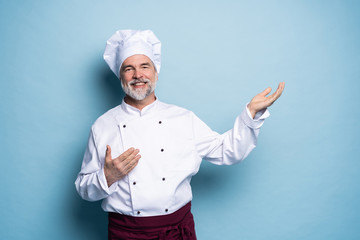 Portrait of a happy chef cook showing copyspace on the palms isolated on light blue background.