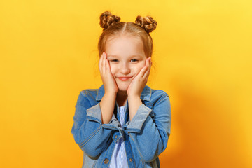 Closeup portrait of a cute attractive little girl on yellow background. Child hands face and looks into the camera.