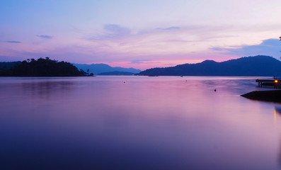 Beautiful violet sunset with reflexions in the motionless ocean - Island and hills in the background - panoramic 