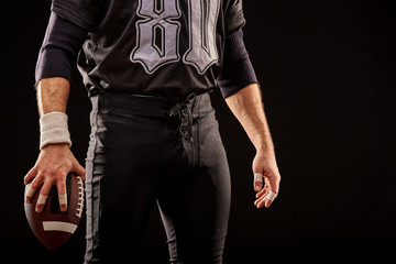 Fototapeta na wymiar Mid section of American football player with ball against black, copy space