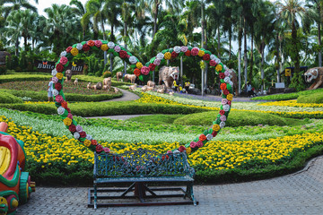 Three seater wooden bench in summer garden full of flowering plants and shrubs.