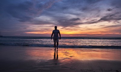 Fototapeta na wymiar A man walks into the water at sunset