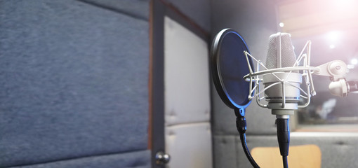 Studio microphone with shock mount and pop filter on professional tripod in acoustic foam room for...