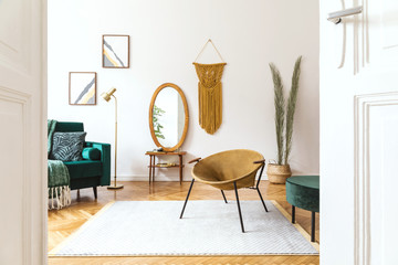 Stylish and elegant interior of living room with design gold armchair, velvet sofa, lamp, poster frames. dressing table with mirror, plants, palm leaves, yellow macrame and accessories. Home decor. 