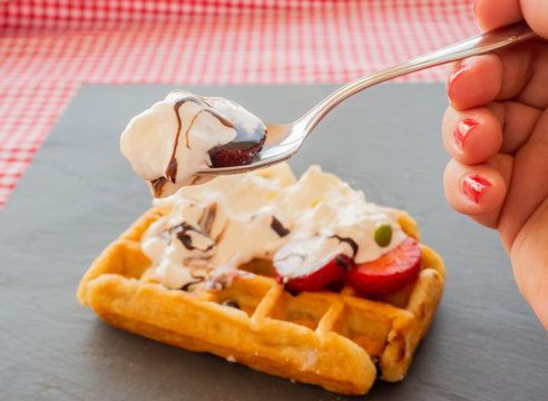 Taking a tablespoon of cream in a waffle with strawberries, whipped cream, chocolate syrup and candy colors