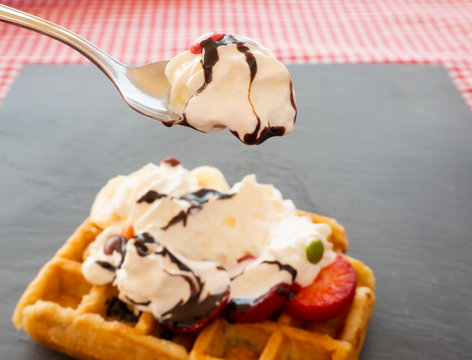 Taking a tablespoon of cream in a waffle with strawberries, whipped cream, chocolate syrup and candy colors