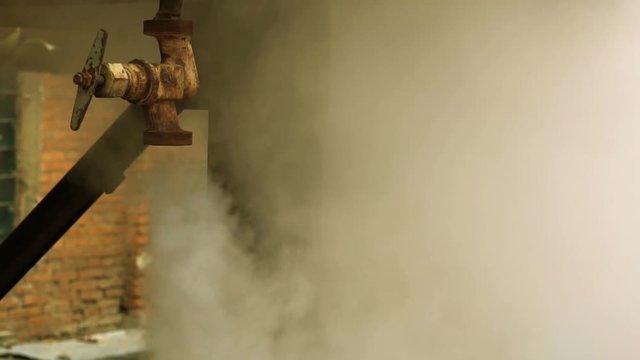Gas or steam leaks from old rusty valve on a high pressure gas pipe. Background to demonstrate environmental pollution, global warming, hazardous production, ecology problems or industrial accident.