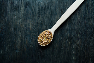 Buckwheat groats in a wooden spoon on a wooden dark background. Wooden spoon with buckwheat grains.