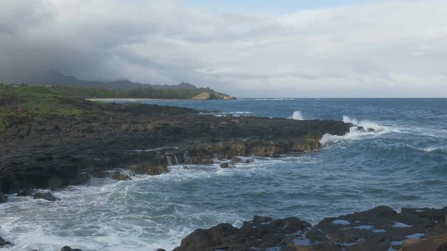 Slow motion (59.94 fps rendered at 29.97) of a wave breaking on lava rock in Poipu, Kauai, Hawaii. Keoniloa Bay and Shipwreck Beach are in the background.