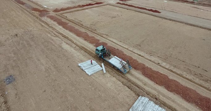 aerial static view of a flatbed truck with crane unloading pillars for house construction 
