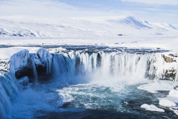 Scenic landscape view of tourist popular attraction Godafoss waterfall in northern Iceland in winter time. Long exposure falling water photo, snow covered mountains on background. 