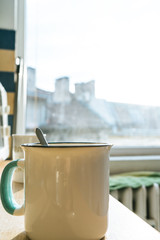 Morning coffee cup with a teaspoon in a kitchen with sunrise and cityscape