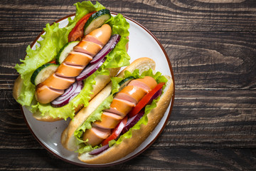 Hot dog with sausage and vegetables on wooden table.