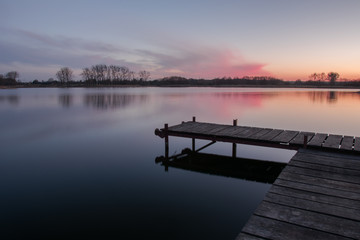 Jetty with planks on a calm lake and pink clouds after sunset