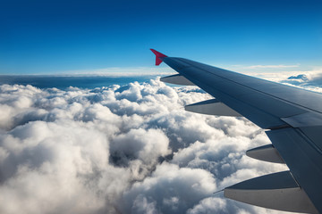 Wing of an airplane flying above the sky with clouds above the ocean