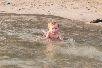 Little boy lying on the beach in the water