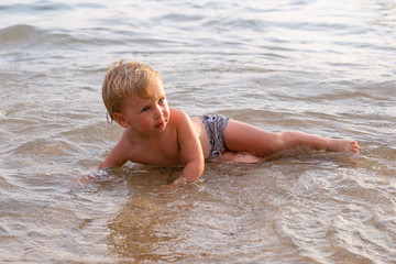 Little boy lying on the beach in the water