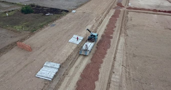 aerial orbital shot of a flatbed truck with crane unloading pillars for house construction 