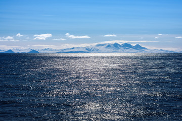 Snow peaks, glaciers and rocks of Aleutian islands in sunny winter day as viewed from ship passing...