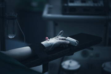 Close up picture of a young patient's hand while the doctors inject the anestetic agent before surgical intervention in a dark, creepy blue lighted surgery block