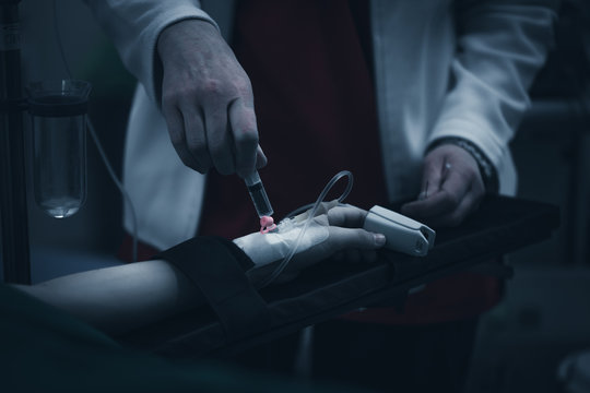 Close up picture of a young patient's hand while the doctors inject the anestetic agent before surgical intervention in a dark, creepy blue lighted surgery block