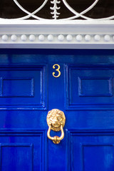 Doorway to house number 3 with the three in bronze and a door knocker in the form of a lion's head on a blue wooden door