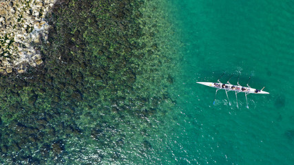 Aerial drone bird's eye view of sport canoe operated by team of young women in tropical caribbean exotic island with emerald and sapphire clear sea
