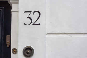 House number 32 with the thirty-two painted in black on a white house wall and door bell