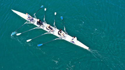 Aerial drone bird's eye view of sport canoe operated by team of young men and women in open ocean sea