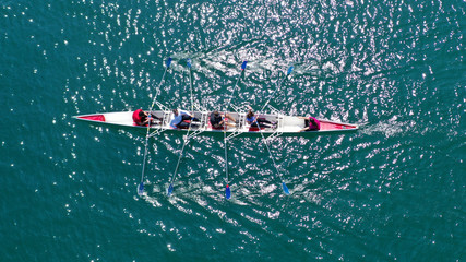 Aerial drone bird's eye view photo of red sport canoe operated by team of young men and women in emerald clear sea