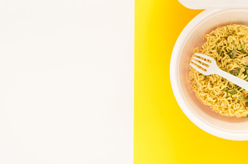 Overhead view of raw instant Asian egg noodles in  plastic bowl with fork and vegetables isolated on white and yellow background. Soft light, close up. Top view of instant noodle. Flat style