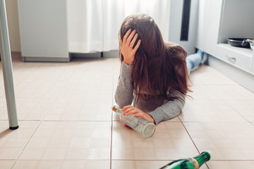 Female alcohol addiction. Young woman woke up on kitchen floor after party surrounded with wine...