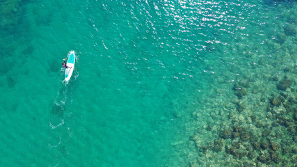 Aerial drone bird's eye view photo of young fit woman practicing paddle board or sup in tropical caribbean sapphire crystal clear calm waters