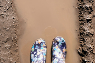 Blue rubber boots splashing in a muddy puddle. Spring, rains concept.